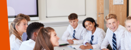 Group of students at a table smiling and looking up at their teacher.